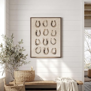 May include: A rectangular wall art print in a dark frame featuring a grid of twelve dark brown horseshoe illustrations arranged in four rows of three on a textured beige background. The artwork is displayed on a white horizontal paneled wall.