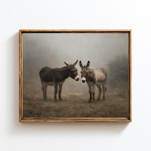 Puede incluir: Impresión enmarcada con dos burros en un campo. Uno es marrón, el otro gris y blanco. Están de pie cerca, tocándose la cabeza. El fondo es un paisaje brumoso y apagado, creando una escena suave.