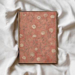 May include: A framed floral print featuring a repeating pattern of white flowers and green stems on a coral background. The artwork is enclosed in a thin, wooden frame. The print has a vintage aesthetic.