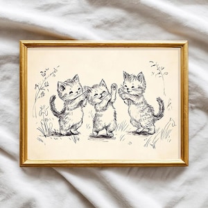 May include: A framed print with a pen and ink illustration of three kittens at play. The image has a vintage feel, with the kittens in a field of grass and flowers. The frame is gold-coloured.