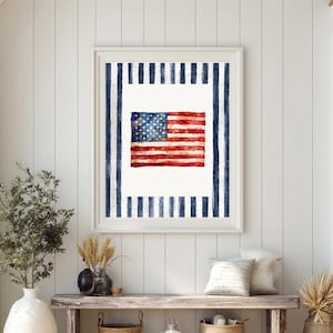 May include: Framed watercolor print of the American flag. The flag features red and white stripes with a blue field of white stars. The print is surrounded by a white border and a blue striped frame, perfect for patriotic decor.