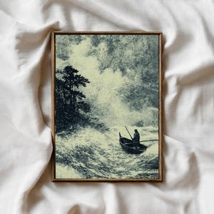 May include: A framed print depicts a lone figure in a small boat navigating turbulent waters. The artwork, in shades of gray and cream, shows a stormy sea, a dark shoreline with trees, and a dramatic sky. The frame is a warm, natural wood tone.