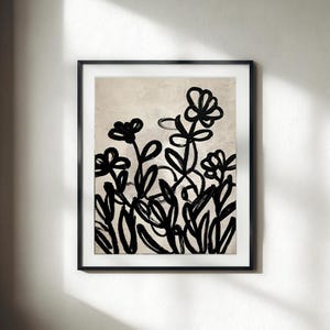 May include: A framed wall art print featuring a black ink illustration of stylized flowers and leaves on a textured beige background. The artwork is enclosed in a thin black frame with a white mat border, displaying bold, expressive brushstrokes.