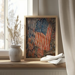 May include: A framed art print featuring an impressionistic painting of the American flag with visible brushstrokes in red, white, and blue, displayed next to a light-colored ceramic vase containing dried botanical stems and a white cloth.