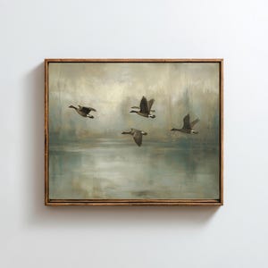 以下が含まれることがあります： 水面を飛ぶ4羽のガチョウを描いた額入りの絵画。このアートワークは、緑、青、茶色の落ち着いた色使いで、木製のフレームに入っています。ガチョウは飛行のさまざまな段階にあり、動きの感覚を作り出しています。