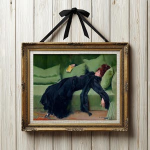 Puede incluir: Una impresión artística enmarcada de una mujer con un vestido negro reclinada en un sofá verde, sosteniendo un libro. La obra de arte está en un marco dorado adornado, suspendido por una cinta y un lazo negros contra un fondo de madera blanca.