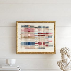 May include: A rectangular wall art piece featuring a woven textile with a grid pattern of red, blue, and beige threads, encased in a thin gold frame. The artwork displays a textured, layered appearance with horizontal and vertical lines.