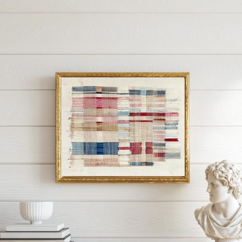 May include: A rectangular wall art piece featuring a woven textile with a grid pattern of red, blue, and beige threads, encased in a thin gold frame. The artwork displays a textured, layered appearance with horizontal and vertical lines.