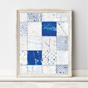 May include: A framed wall art piece featuring a grid of square patches in shades of white and deep blue. The design displays various textures and patterns, including solid blue squares, cross-hatched lines, and dotted motifs, all joined by visible stitching.