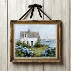 May include: Framed coastal landscape art featuring a white house with a gray roof, blue hydrangeas, and a sailboat on the water. The artwork is in a gold ornate frame and is suspended by a black ribbon.