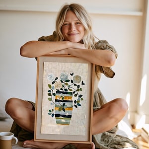 May include: A framed art print featuring a vase with horizontal stripes in shades of blue, green, and yellow, filled with white and cream-colored flowers, green leaves, and two small black butterfly silhouettes on a textured, light-colored background.
