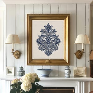 May include: A framed print featuring a blue and white floral design. The print is in a gold frame and hangs above a white mantel. Two sconces with cream-colored shades flank the print. Decorative items, including a bowl and vase, are on the mantel.