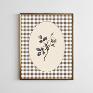 May include: Framed botanical print featuring a detailed illustration of a rose branch with leaves and a single bloom. The artwork is set within an oval cream-colored space, against a brown and white checkered background, and framed in gold.