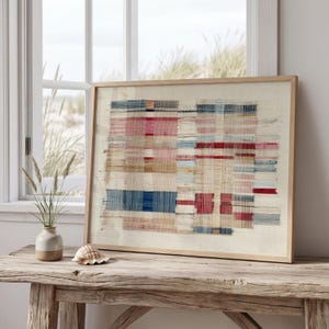 May include: A framed rectangular wall art piece featuring a woven textile design with horizontal and vertical threads in shades of blue, red, pink, and beige. The artwork displays a grid-like pattern of intersecting colored lines on a light background.