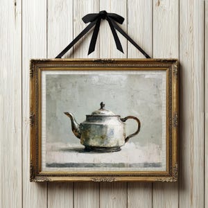 May include: A framed oil painting depicting a metallic teapot with a lid and handle, rendered in shades of silver, gray, and white. The artwork is enclosed in an ornate gold frame and is suspended by a black ribbon tied in a bow at the top.
