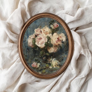 May include: Oval framed painting of a bouquet of pale pink roses with green foliage on a blue backdrop. The wooden frame has a warm, brown hue. The artwork is set against a backdrop of a white, textured fabric.