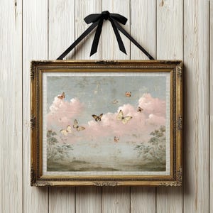 Può includere: Una stampa artistica da parete rettangolare in una cornice dorata decorata che raffigura una scena del cielo con soffici nuvole rosa, alberi verdi sul fondo e diverse farfalle in volo. Un nastro nero è legato a fiocco in alto per appenderla.