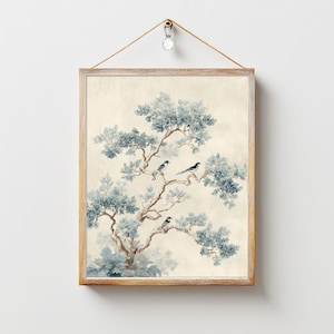 Op de afbeelding: Ingelijste kunstdruk met een boom met blauwgroen blad en drie vogels die op zijn takken zitten. Het kunstwerk heeft een vintage esthetiek, met een lichtbeige achtergrond en een natuurlijke houten lijst. De print wordt opgehangen met een decoratief koord.
