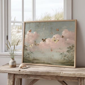 Könnte beinhalten: Ein rechteckiger gerahmter Kunstdruck, der eine Landschaft im Vintage-Stil mit zartrosa Wolken, gedämpftem grünem Blattwerk und mehreren fliegenden Schmetterlingen zeigt. Das Bild hat eine verwitterte Textur und einen hellen Holzrahmen.