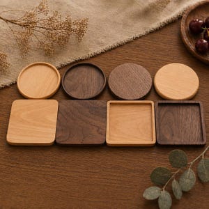 Puede incluir: Un surtido de posavasos de madera en varias formas y tonos marrones. Los posavasos incluyen diseños redondos y cuadrados, con tonos de madera claros y oscuros. La disposición está sobre una superficie de madera.