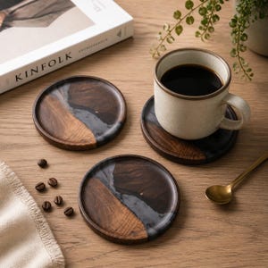May include: Three circular wooden coasters with a dark brown and grey resin inlay. A beige mug with dark liquid sits on one coaster. Coffee beans and a gold spoon are also visible.