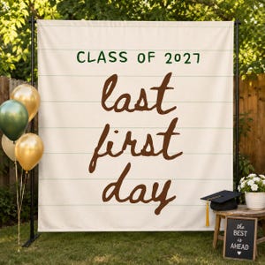 May include: A cream-colored fabric backdrop featuring horizontal lines and the dark green text "CLASS OF 2027" above the large brown script text "last first day". The backdrop is mounted on a black metal stand with gold and green balloons.