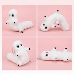 May include: Four images of a white plush creature with black eyes and small black feet. The creature has a long, worm-like body and a rounded head. Each image shows the creature in a different pose against a pink background.