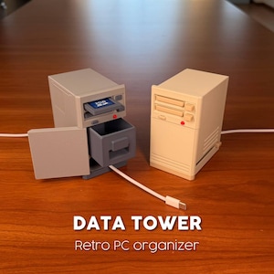 May include: Two retro PC tower organisers in beige and grey. One unit features an open side door, a pull-out drawer, and a slot containing a 2GB SD card. The other unit is closed with two front drive bays and a red indicator light. Text reads DATA TOWER.
