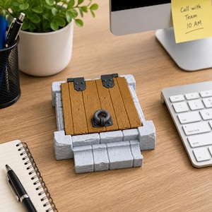 May include: A decorative object shaped like a small wooden door with a dark metal ring knocker and black hinges, set into a light gray stone frame with a short flight of steps at the base. The door features a vertical wood grain texture.