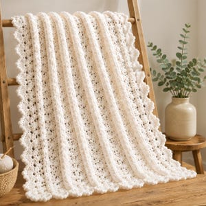 May include: A cream-colored crocheted blanket featuring a textured pattern of vertical raised ribs alternating with delicate openwork lace sections. The edges of the blanket are finished with a scalloped border, creating a soft and uniform appearance.