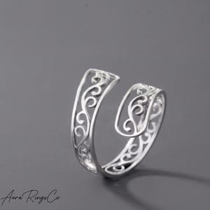 May include: A silver-toned open ring featuring a delicate, continuous filigree scrollwork pattern throughout the band. The design consists of interconnected swirling lines that create an airy, cutout effect, with the ring ends slightly offset.