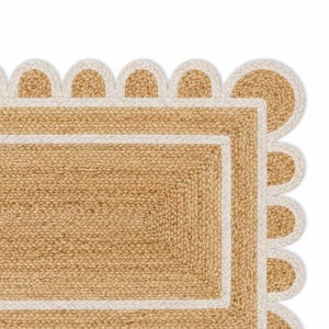 K&ouml;nnte beinhalten: Ein rechteckiger Teppich aus geflochtenen, naturfarbenen beigen Jutefasern. Der Teppich verf&uuml;gt &uuml;ber einen breiten wei&szlig;en Rand und einen dekorativen, wellenf&ouml;rmigen Abschluss, der mit einer passenden wei&szlig;en geflochtenen Kante versehen ist.