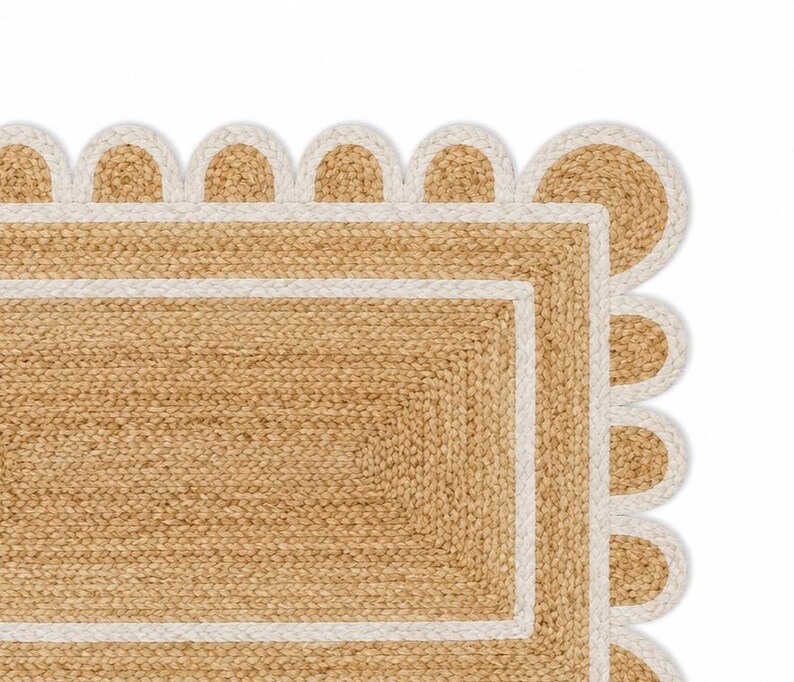 K&ouml;nnte beinhalten: Ein rechteckiger Teppich aus geflochtenen, naturfarbenen beigen Jutefasern. Der Teppich verf&uuml;gt &uuml;ber einen breiten wei&szlig;en Rand und einen dekorativen, wellenf&ouml;rmigen Abschluss, der mit einer passenden wei&szlig;en geflochtenen Kante versehen ist.