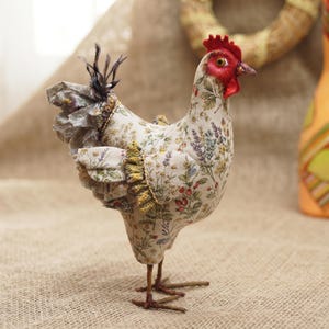 May include: A fabric chicken figurine featuring a cream-colored base with a botanical print of lavender, wildflowers, and berries. The figure has a bright red comb and wattle, dark brown wire legs, and ruffled fabric wing accents.
