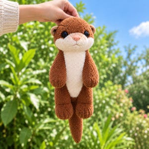 Op de afbeelding: Een otter-knuffel met bruine, gestructureerde vacht, een crèmekleurig gezicht en borst, kleine ronde oortjes en grote zwarte ogen. Het knuffeldier heeft een zachte, pluizige uitstraling met een lange staart en een kleine roze neus.