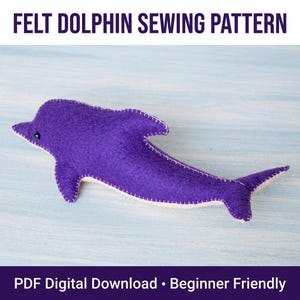 Puede incluir: Un delfín de fieltro morado con bordes cosidos en punto de festón blanco y un pequeño ojo de cuenta negra. El texto FELT DOLPHIN SEWING PATTERN aparece arriba y PDF Digital Download • Beginner Friendly aparece abajo en la imagen.