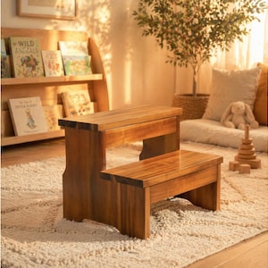 May include: A two-step wooden stool with a natural finish. The stool is made of solid wood and has a rectangular shape. The steps are approximately 12 inches high and 18 inches wide. The stool is designed for children.