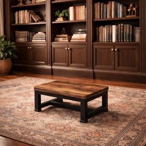 May include: A rectangular coffee table with a dark wood grain top and black legs. The table is set on a patterned rug in front of a dark wood bookcase filled with books.