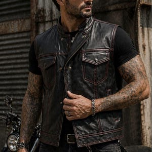 Male rider wearing a black leather biker vest with red contrast stitching, snap front closure, chest flap pockets and side hand pockets.