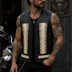 May include: A black leather vest featuring vertical panels of cream-colored snakeskin texture on the front. The sleeveless garment has a central zipper closure and horizontal snakeskin accents along the lower hem, providing a distinct contrast.