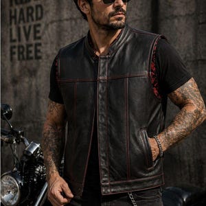 Male rider wearing a black biker vest with red contrast stitching and a red patterned inner lining beside a motorcycle.