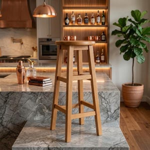 Könnte beinhalten: Ein hoher Barhocker aus hellem Holz mit runder Sitzfläche und Fußstütze. Der Hocker hat ein schlichtes Design und steht in einer Küche mit Marmortheke und kupferfarbener Beleuchtung. Die Höhe ist für eine Bar geeignet.