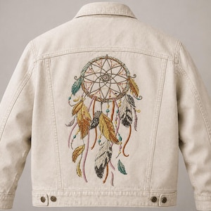 May include: Cream-colored denim jacket featuring an embroidered dreamcatcher design on the back. The dreamcatcher is detailed with feathers in shades of gold, brown, and black, with accents of blue and pink. The jacket has a classic button-up design with pockets.