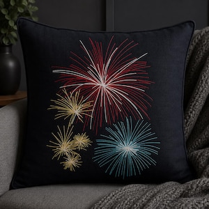 Könnte beinhalten: Quadratisches, marineblaues Zierkissen mit einem gestickten Feuerwerksdesign. Die Feuerwerkskörper sind in roter, weißer, gelber und blauer Farbe dargestellt. Das Kissen hat einen dunkelblauen Rand.