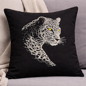 May include: Black square throw pillow featuring an embroidered leopard design. The leopard is depicted in white thread with yellow eyes, set against a solid black background. The pillow is a decorative accent for a sofa or bed.