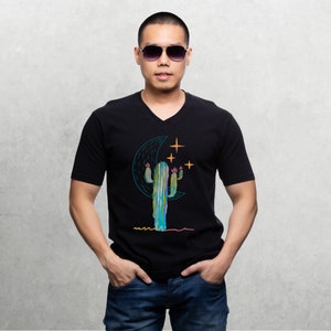 May include: A black v-neck t-shirt with a graphic of a cactus, a crescent moon, and stars. The cactus is green, blue, and pink, and the moon is blue. The stars are yellow.