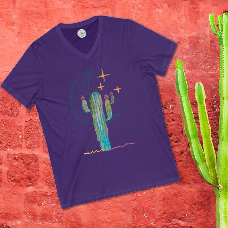 May include: Purple V-neck t-shirt with a graphic of a green cactus with pink flowers under a crescent moon and stars.