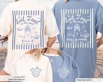 May include: Ivory and blue t-shirts with a beach-themed design. The back of the ivory shirt says "Last Toast on the Coast" with champagne glasses and seashells. The blue shirt says "Amily's Bachelorette" with the same design. The front of the ivory shirt says "The Bride".