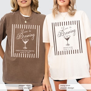 May include: Two short-sleeve crewneck t-shirts, one brown and one ivory, each featuring a graphic of a martini glass with the text Love is Brewing. The brown shirt includes the text EMILY'S BACHELORETTE MIAMI FL 2026, while the ivory shirt says BRIDE TO BE MIAMI FL 2026.