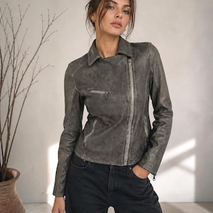 Peut inclure: Veste en cuir grise avec fermeture éclair et plusieurs poches. La veste a un col classique et une finition vieillie. Le modèle porte un jean noir. L'esthétique générale est décontractée et élégante.
